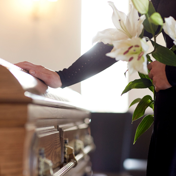woman holding flowers while leaning on coffin during funeral