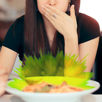 Young woman holding hand over her mouth with bowl of glowing green food in front of her
