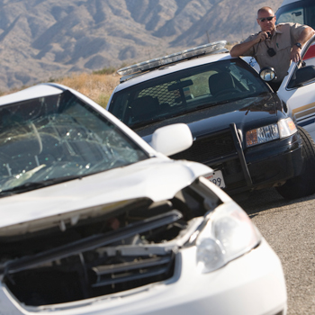 Wrecked white car on highway with police officer standing outside his squad car in background