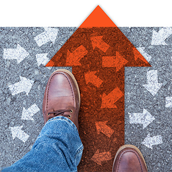 Man's booted feet walking on bright orange arrow over asphalt covered with white arrows